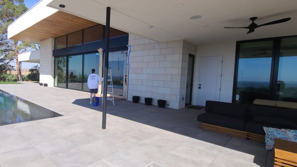 All Shades of Painting crew member in branded shirt working on a modern Eagle Idaho home patio with infinity pool