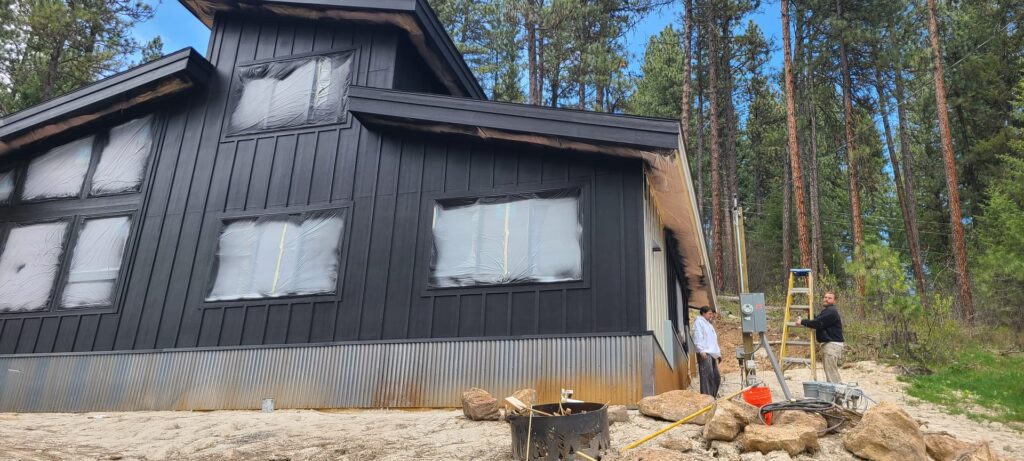 All Shades of Painting crew working on a freshly painted black board and batten mountain home exterior with windows masked for finish work